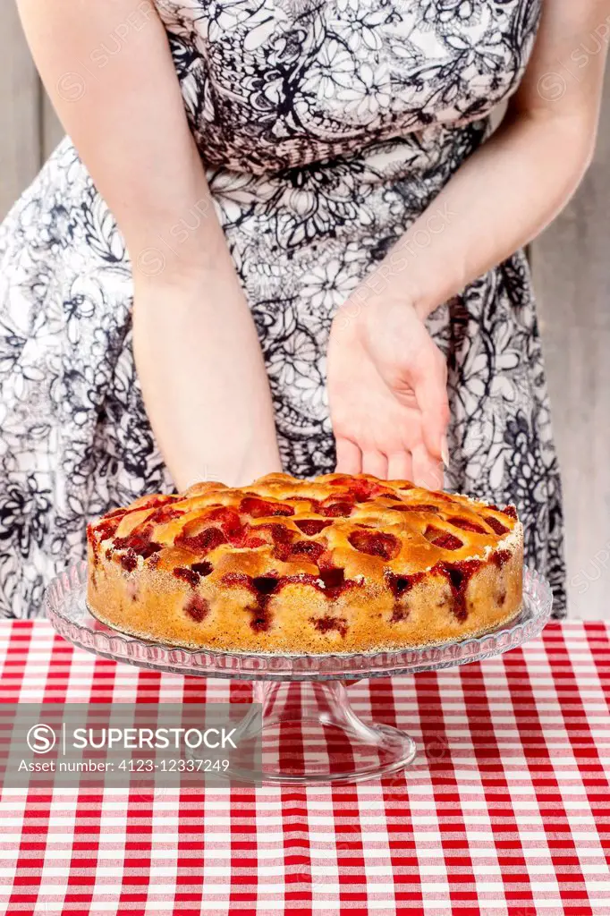 Woman holding cake stand with strawberry cake. Birthday party setting. Selective focus.