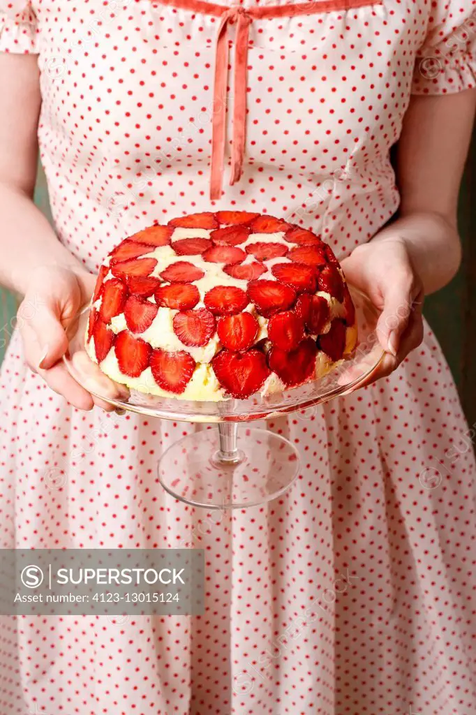Woman holding strawberry cake on cake stand. Party dessert