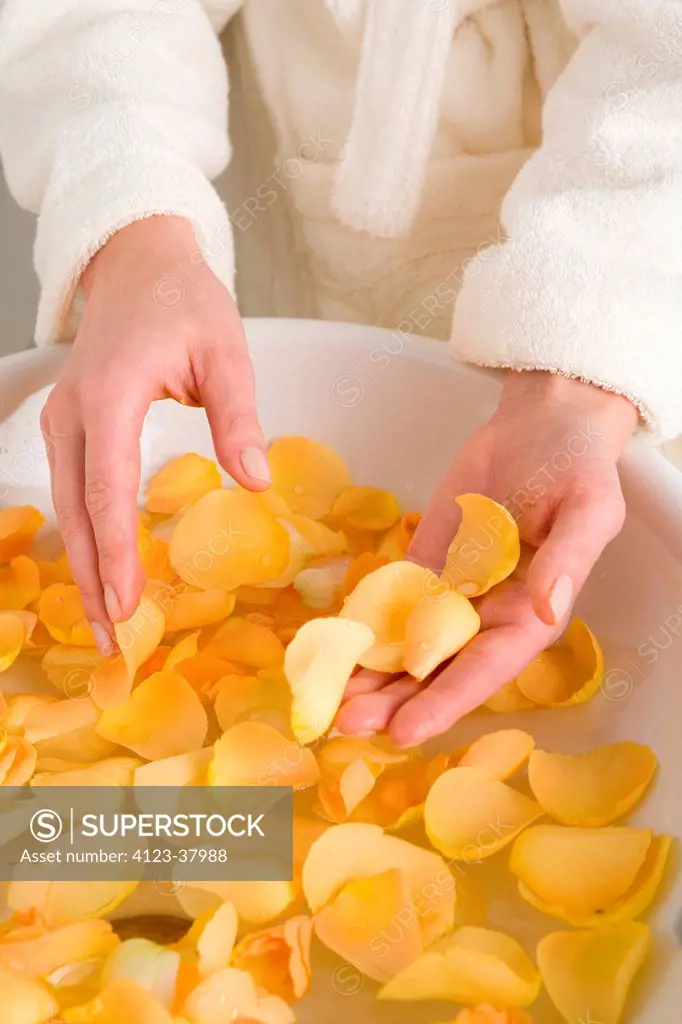 Woman soaking hands in water with flower petals.