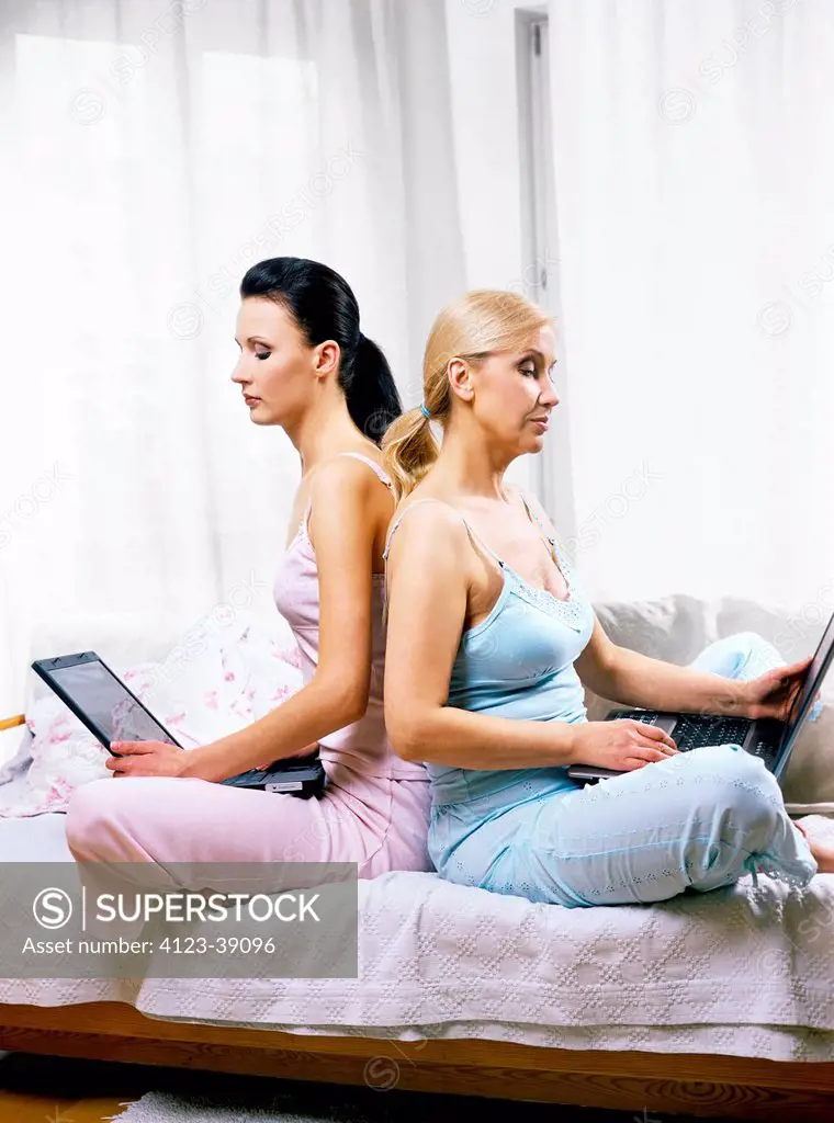 Mother and daughter sitting on the sofa and working with laptops