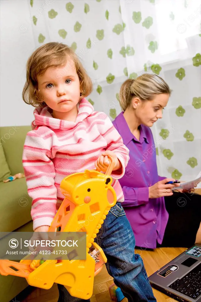 Young woman working on a laptop while looking after a child.