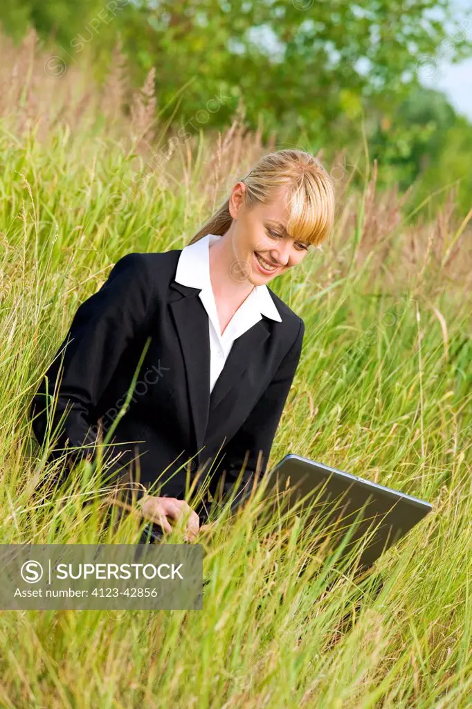 Young woman using notebook on a meadow.
