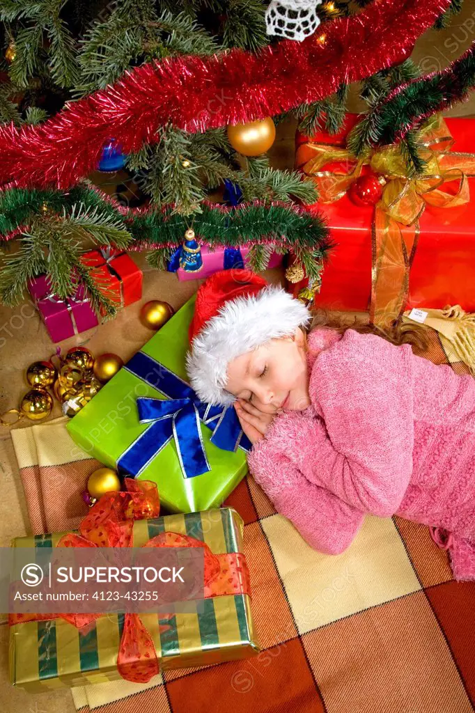 Girl sleeping under Christmas tree.