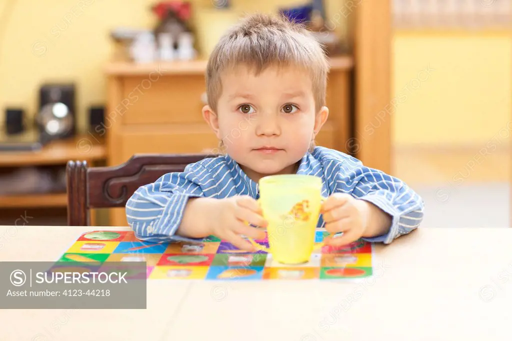 Little boy sitting at dinner table, drinking water from baby cup.