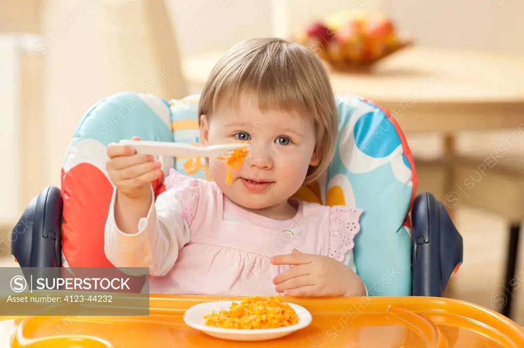 Girl sitting in baby chair, eating carrot salad.