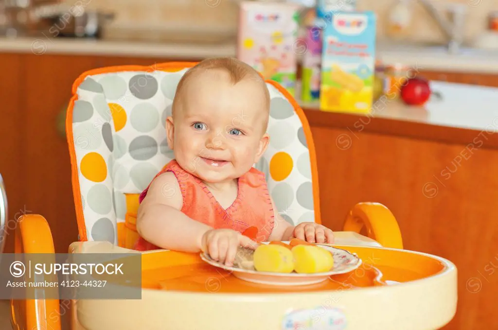 Girl sitting in baby chair, eating dinner.