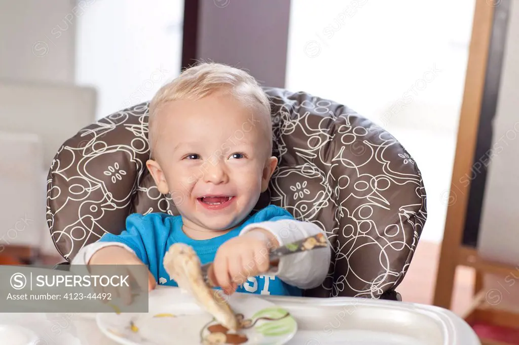 Cute two year old boy sitting in baby-chair, eating lunch.