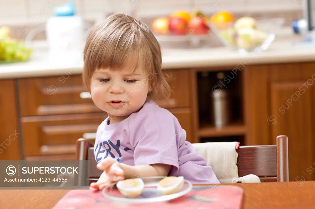 Cute two year old girl eating at the dinner table.