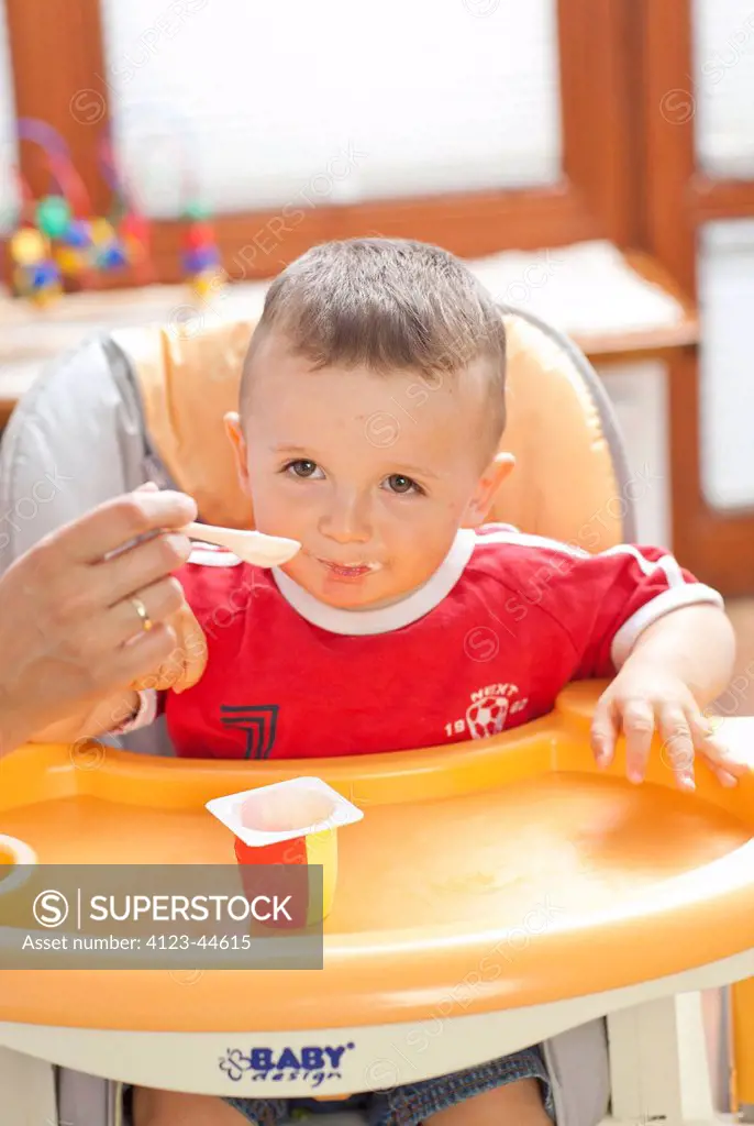 Boy sitting in baby-chair, eating yogurt.