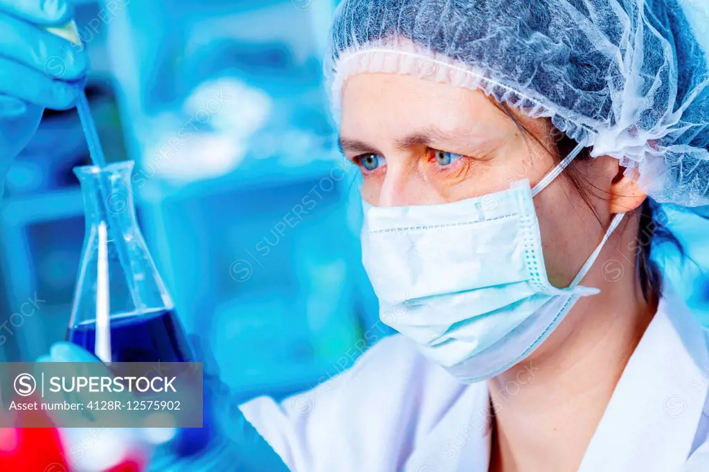 Female chemist wearing face mask holding a conical flask.