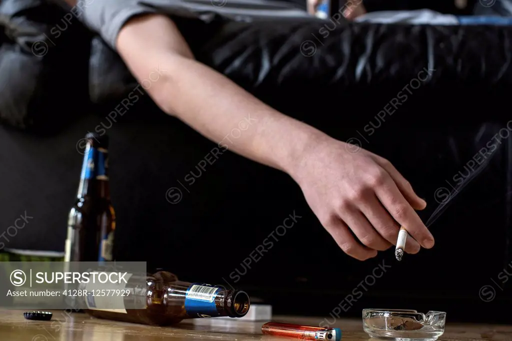 Person holding cigarette with beer bottles on the floor.