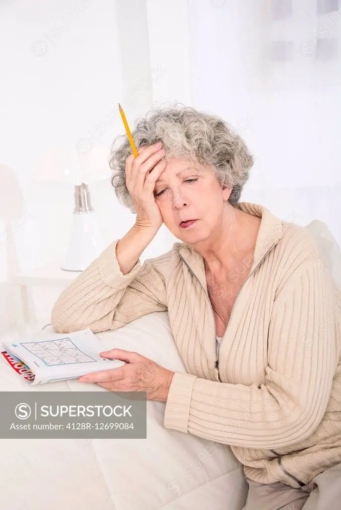 MODEL RELEASED. Senior woman holding a puzzle book with her hand on her head.