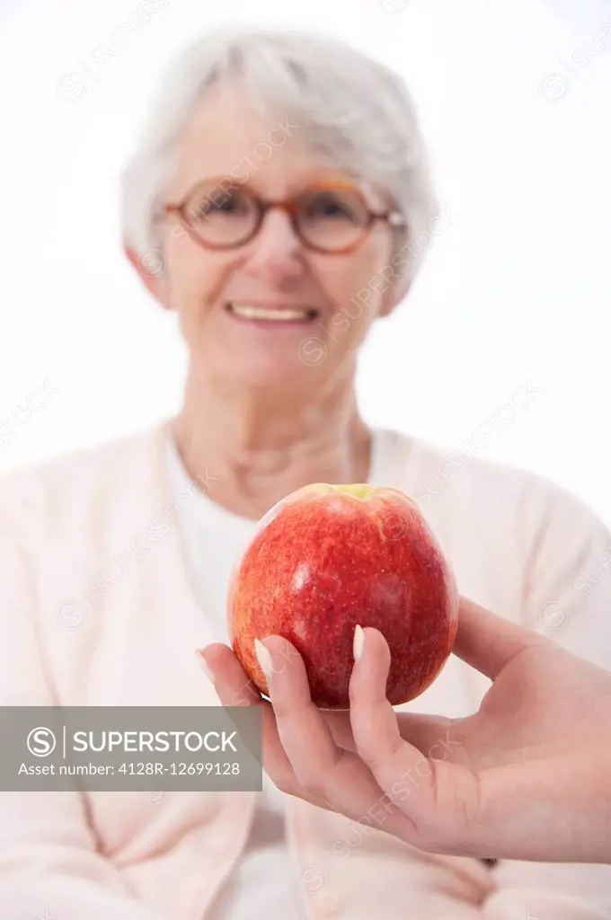 MODEL RELEASED. Healthy eating. Senior woman with a person holding an apple in the foreground.