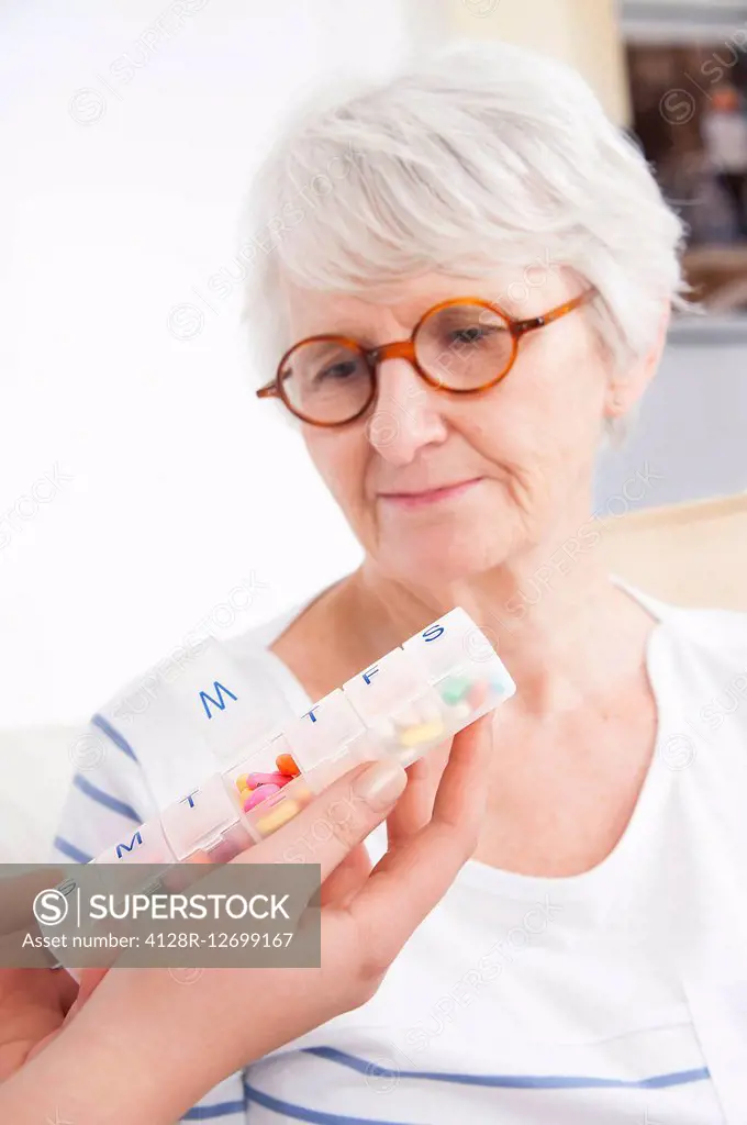 MODEL RELEASED. Person holding a pill container with a senior woman watching.