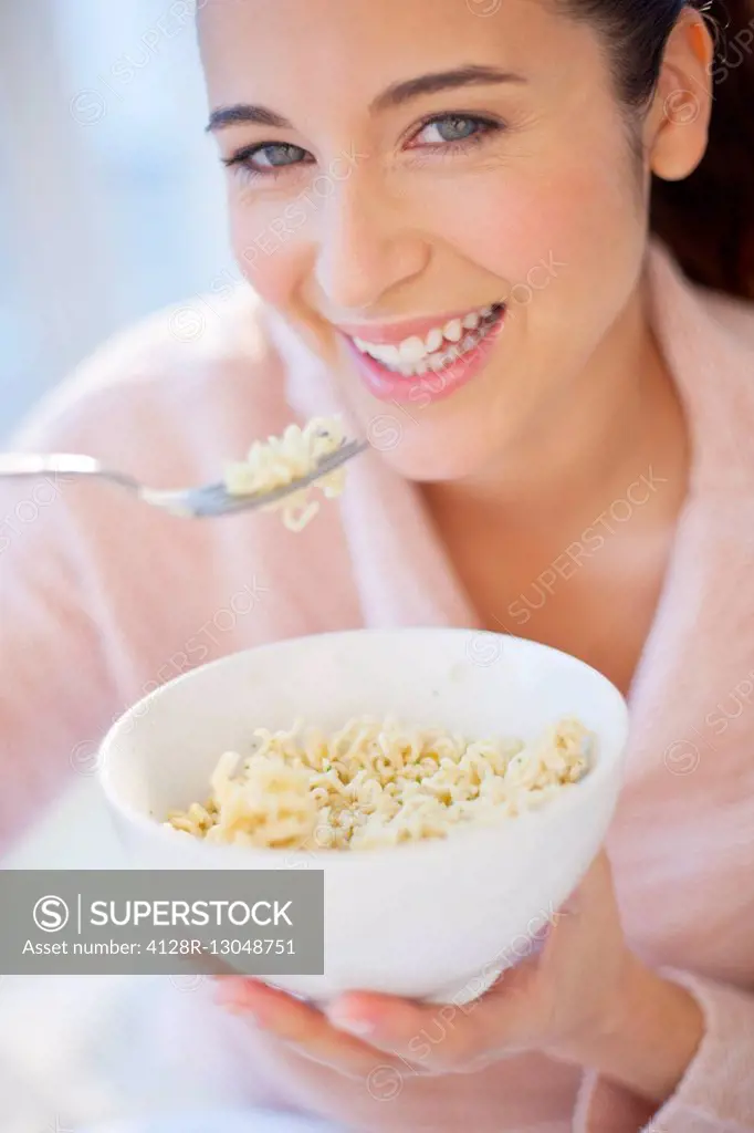 MODEL RELEASED. Woman eating bowl of noodles, smiling.