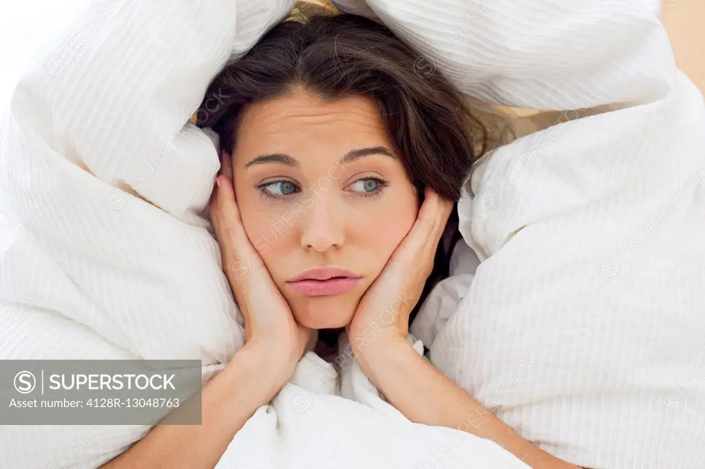 MODEL RELEASED. Woman in bed under the bedclothes with her hands on her chin.