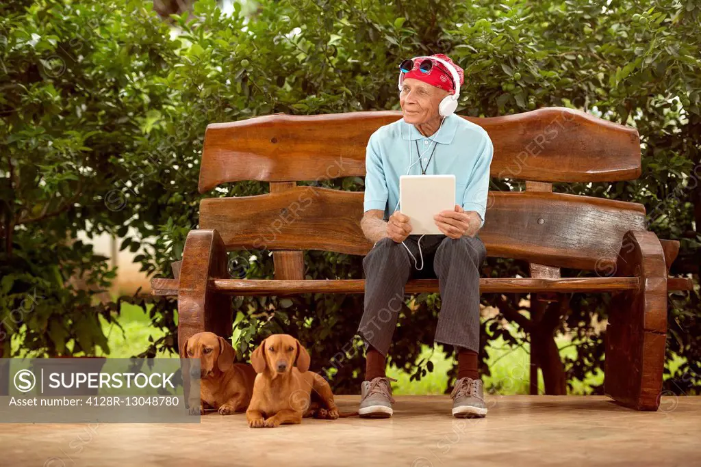 MODEL RELEASED. Senior man sitting on a bench listening to music with his dogs.