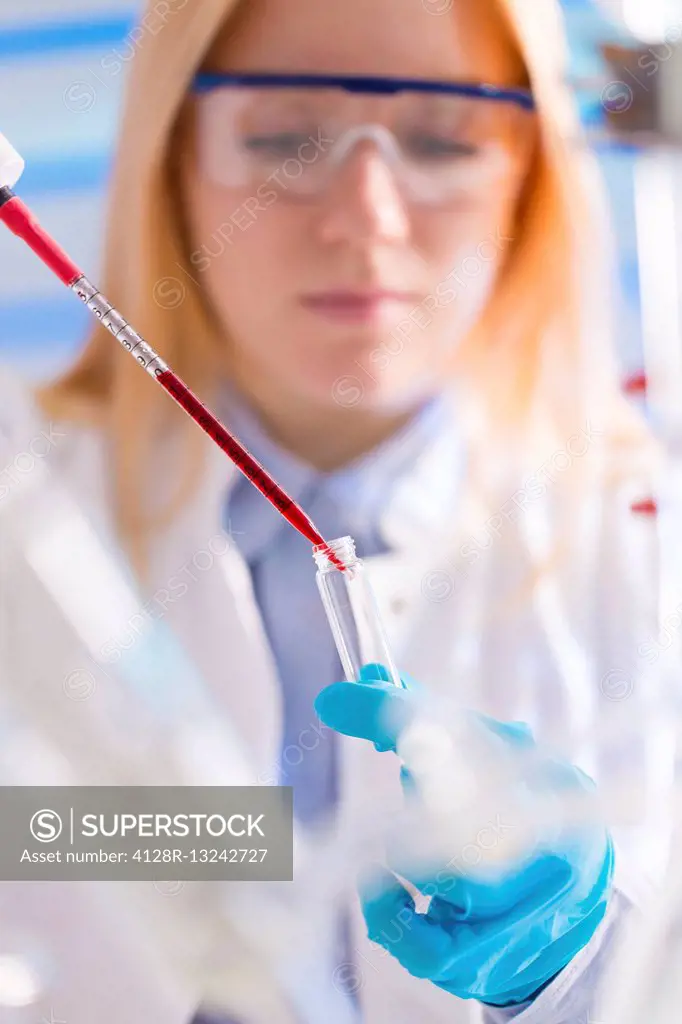 Female lab technician dripping chemical into test tube with pipette.