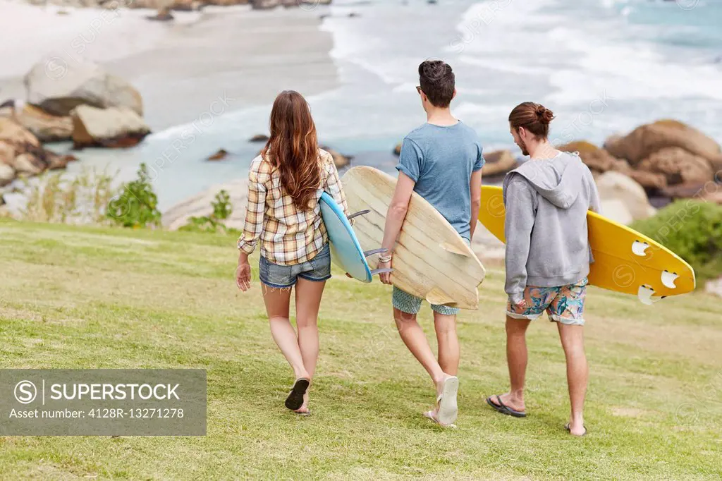 MODEL RELEASED. Three young adults walking towards beach with surfboards.