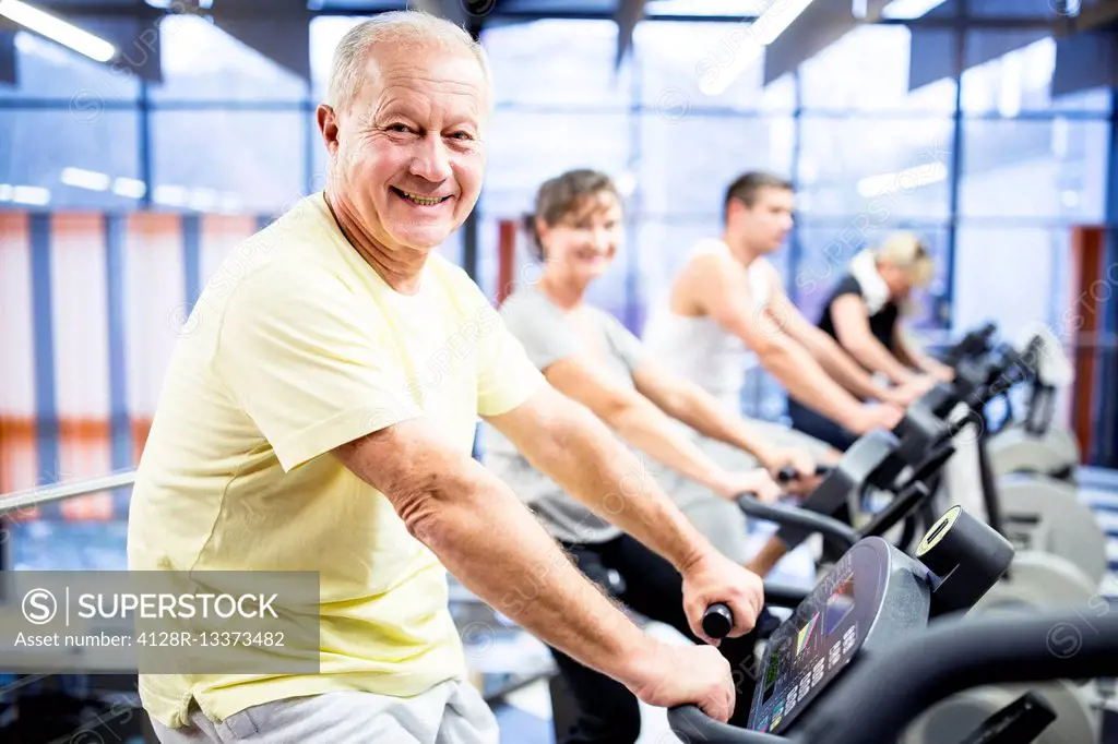 MODEL RELEASED. Senior man exercising on stationary bike in gym.