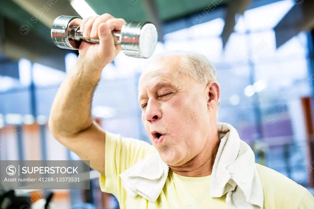 MODEL RELEASED. Exhausted senior man holding dumbbell in gym.