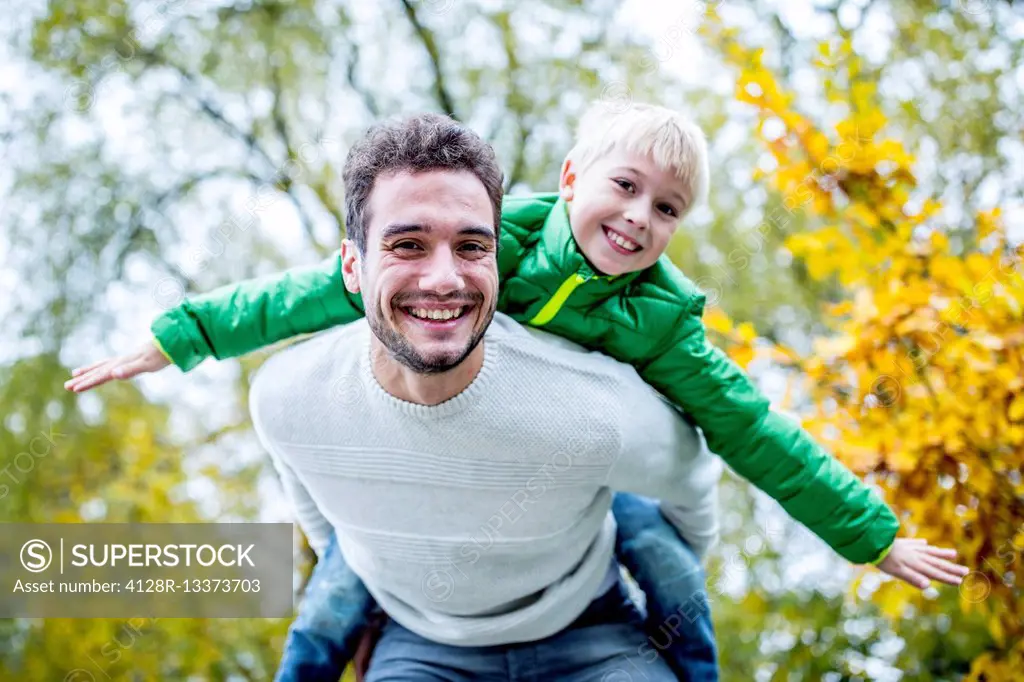 MODEL RELEASED. Father carrying son piggyback in autumn, smiling, portrait.