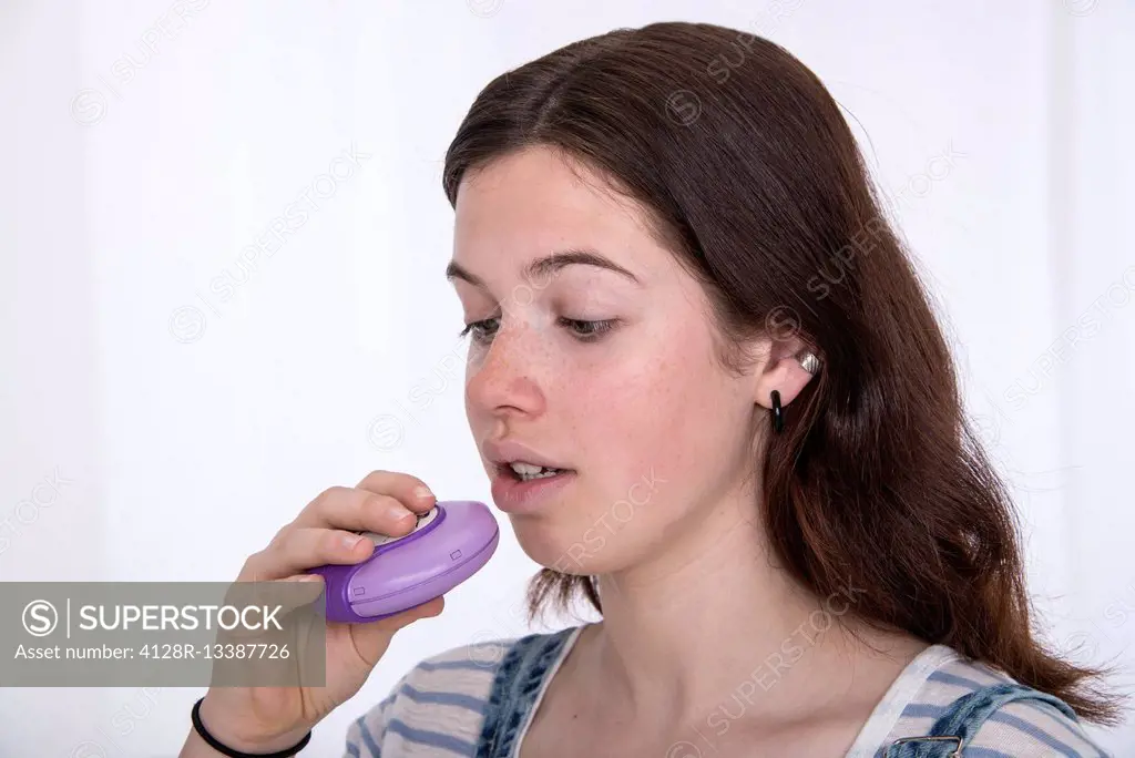 MODEL RELEASED. Teenage girl using asthma inhaler.