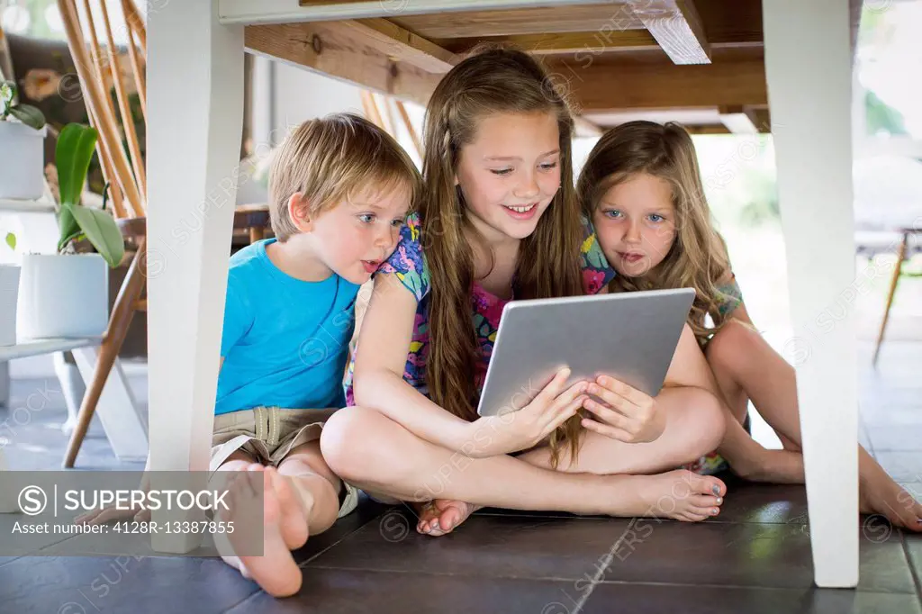MODEL RELEASED. Three siblings under table with digital tablet.