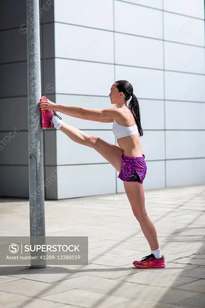MODEL RELEASED. Young woman stretching leg against post.
