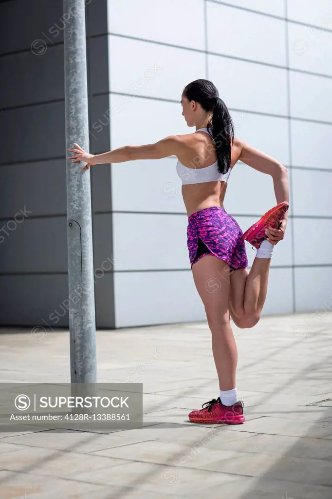 MODEL RELEASED. Young woman stretching leg muscles.