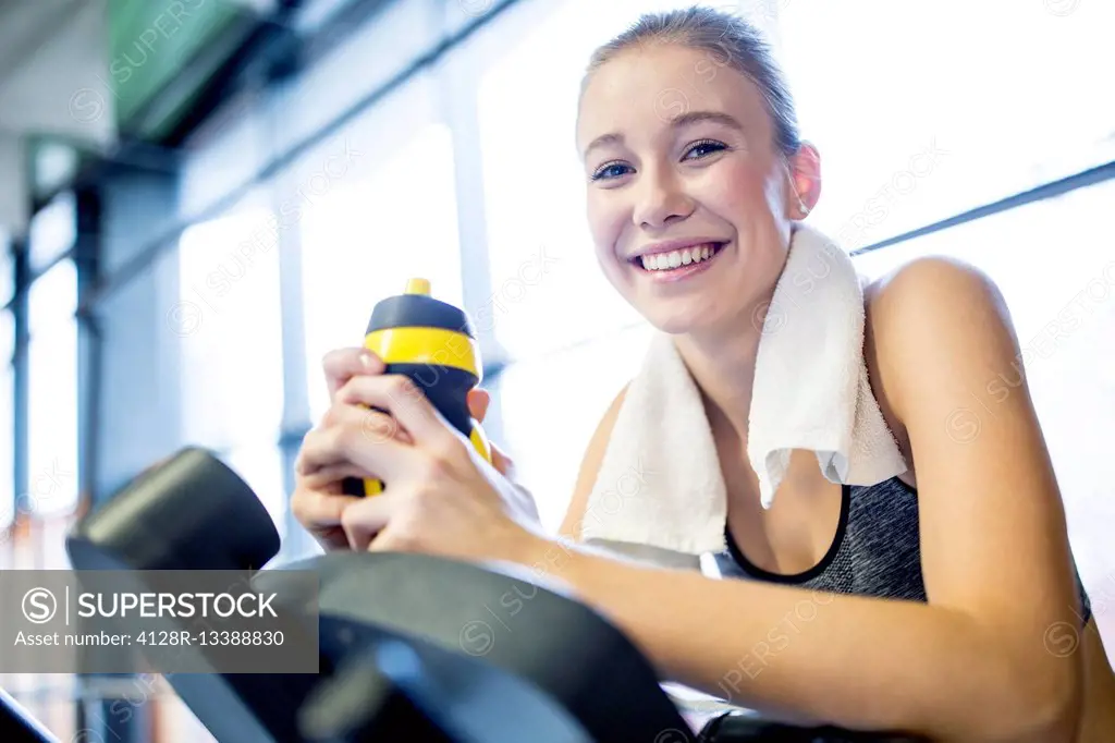 MODEL RELEASED. Young woman holding water bottle while working out in gym, smiling, portrait.