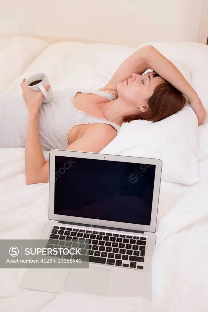 MODEL RELEASED. Exhausted woman in bed with laptop and black coffee.