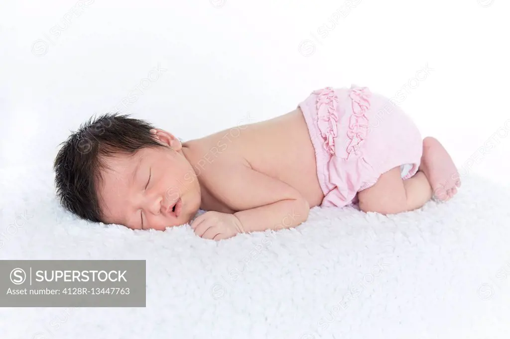 MODEL RELEASED. Newborn baby girl in pink nappy, asleep.