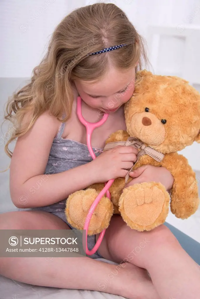 MODEL RELEASED. Girl using stethoscope with teddy bear.