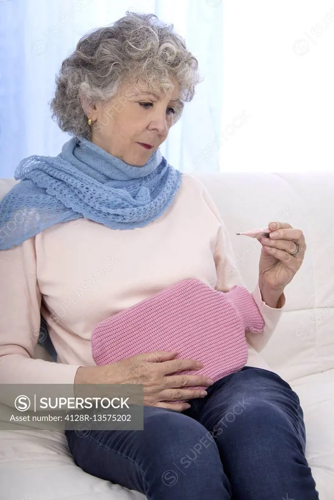 MODEL RELEASED. Woman with hot water bottle and thermometer.