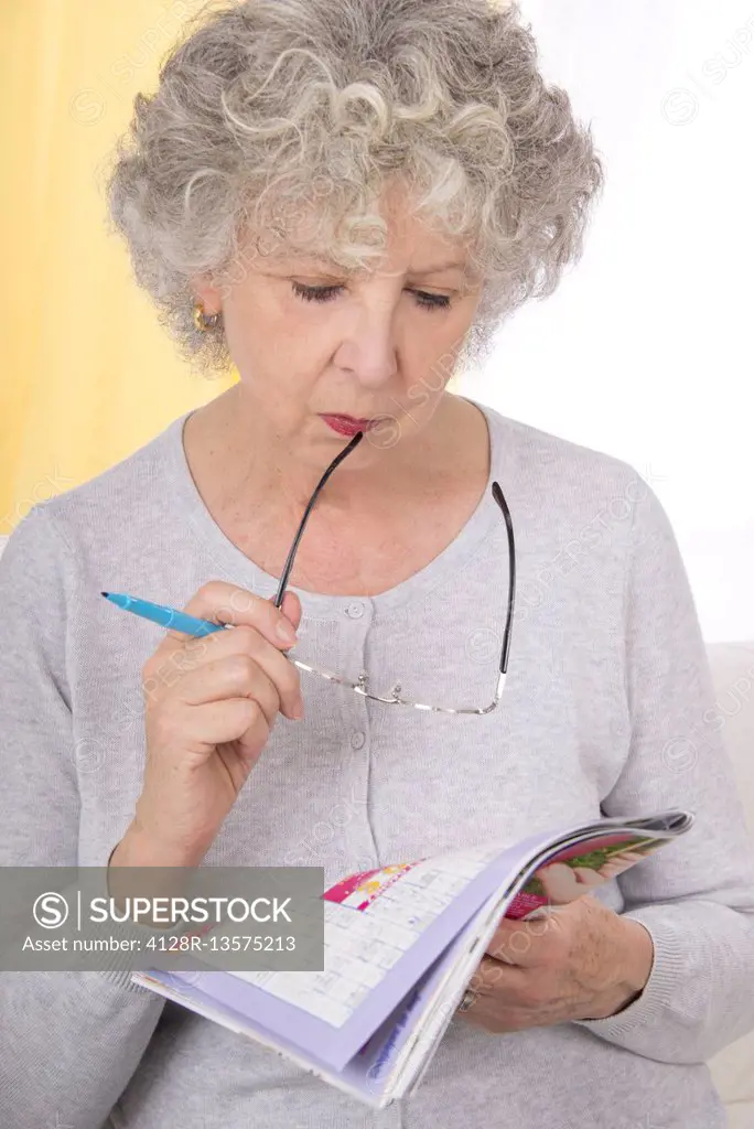 MODEL RELEASED. Woman reading magazine holding glasses.