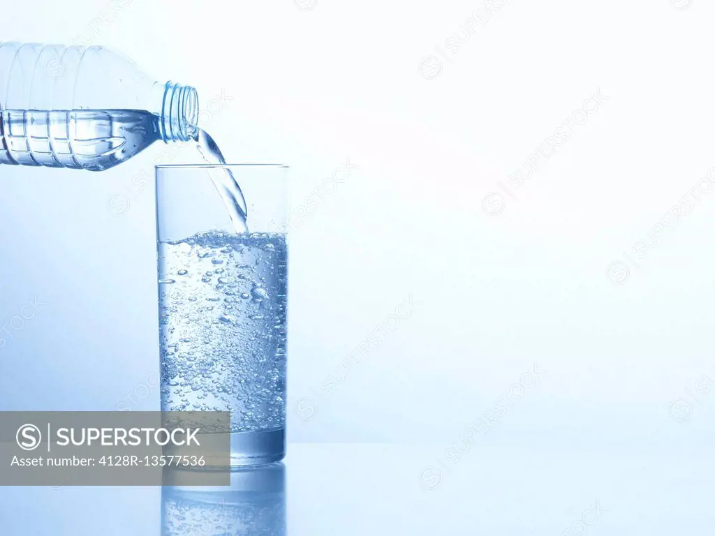 Pouring water from a bottle into a glass, studio shot.