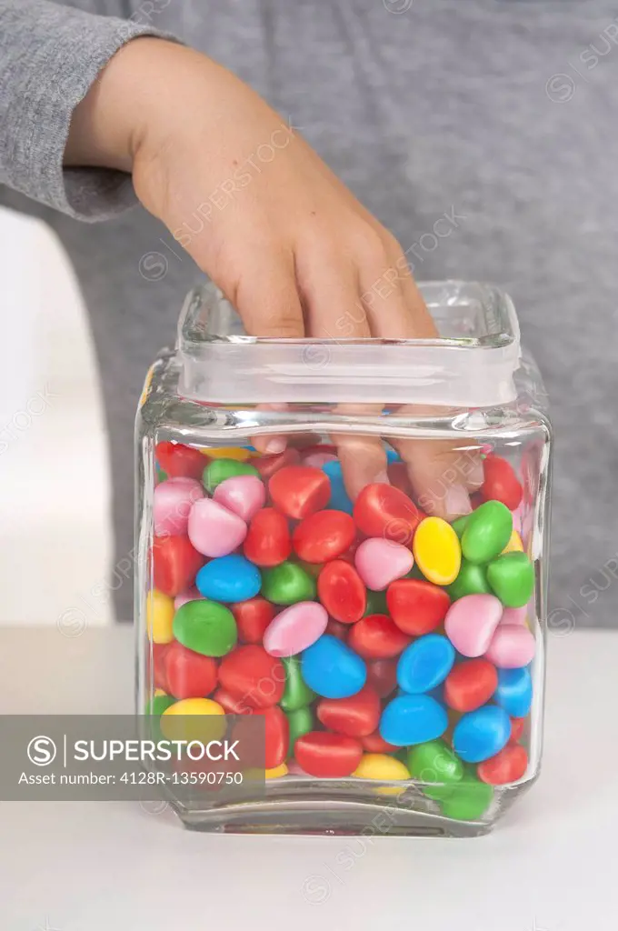 MODEL RELEASED. Child reaching into jar of multicoloured sweets