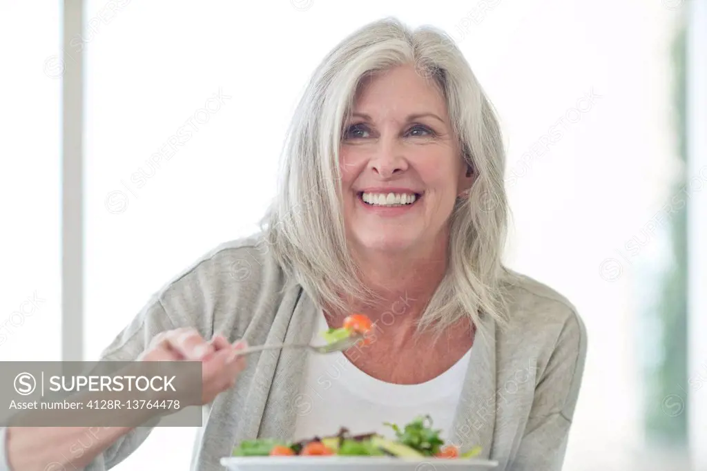 Senior woman eating salad, smiling.