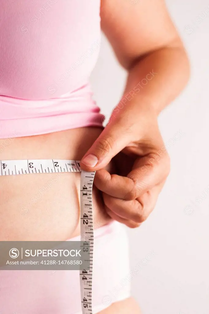 Woman measuring waist with tape measure - SuperStock