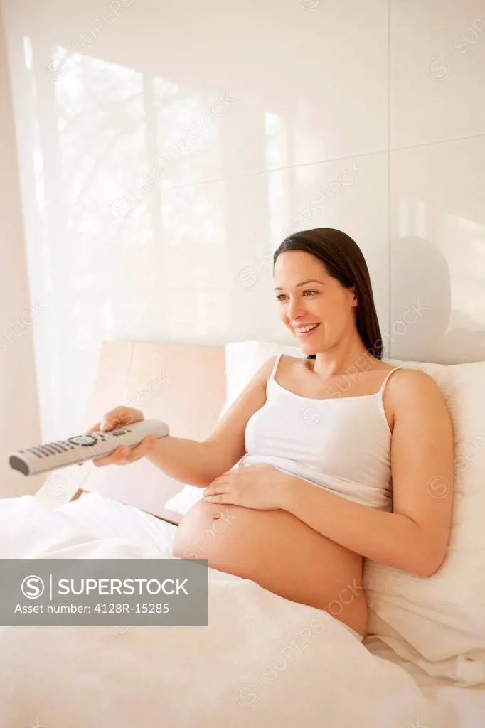 Pregnant woman watching TV in bed.
