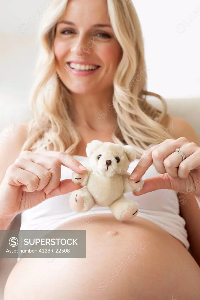 MODEL RELEASED. Pregnant woman with a teddy bear on her bump. She is 8 months pregnant.