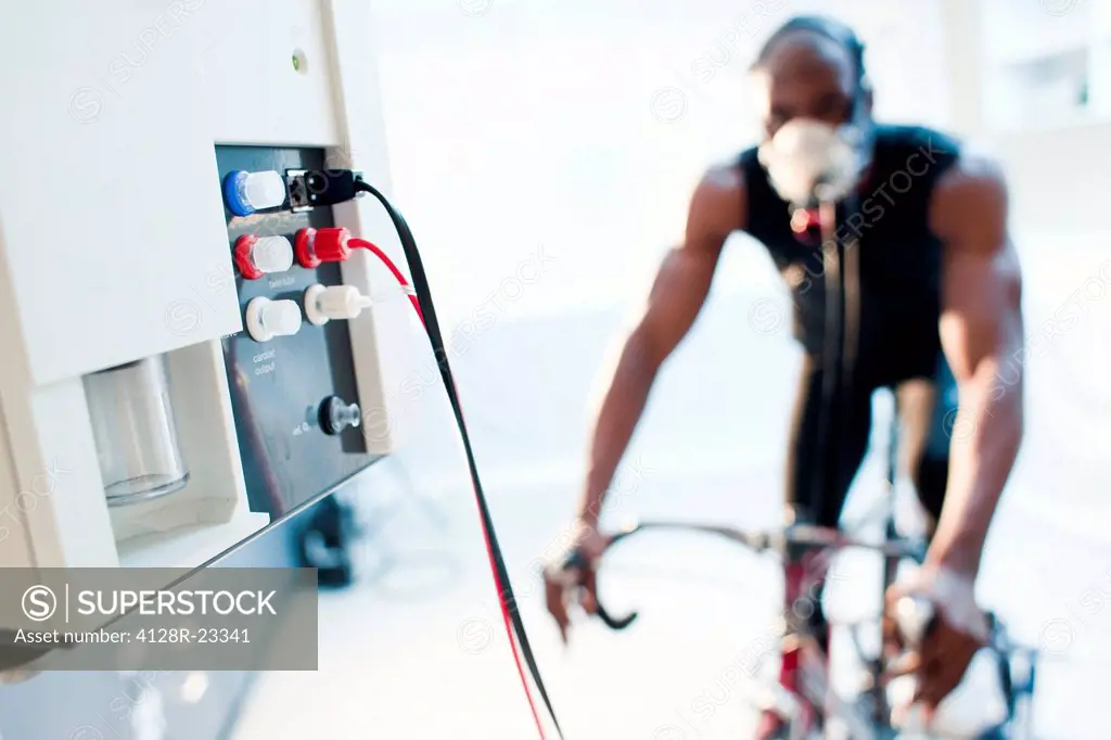 MODEL RELEASED. Performance testing. Athlete riding an exercise bike while his performance and oxygen consumption are measured.