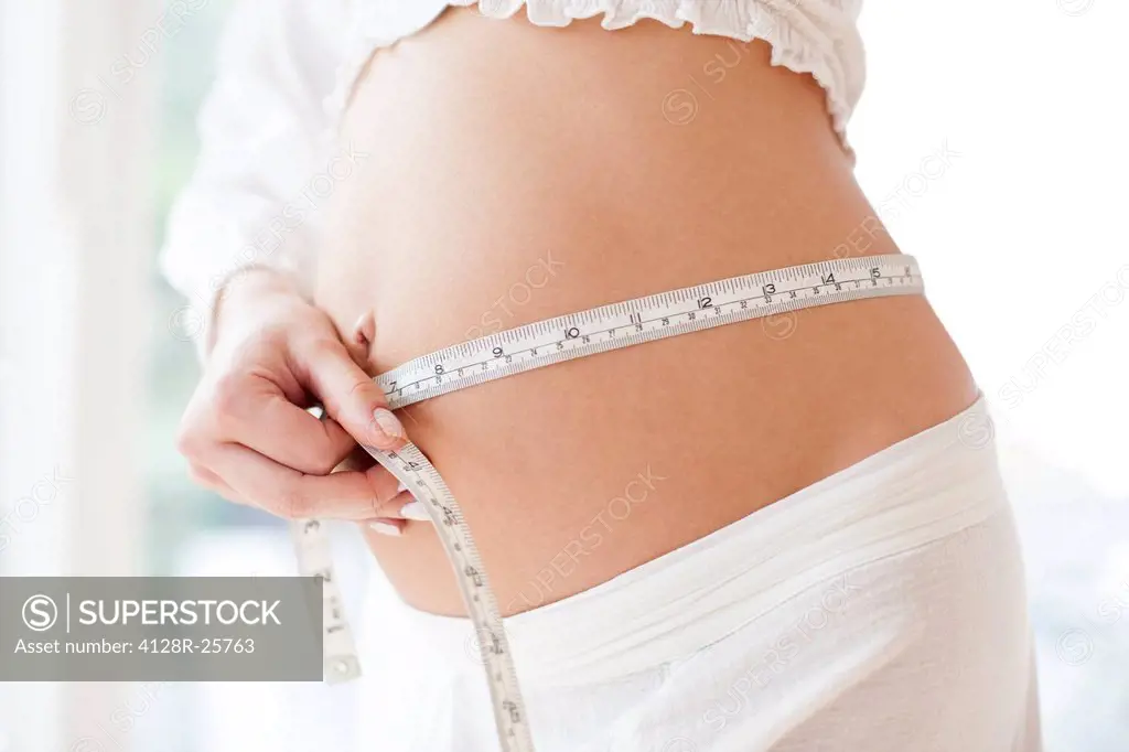 MODEL RELEASED. Pregnant woman measuring her abdomen.