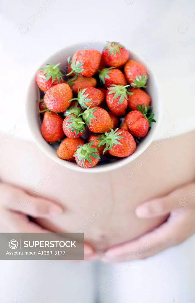 Pregnant woman eating strawberries. She is eight months pregnant.