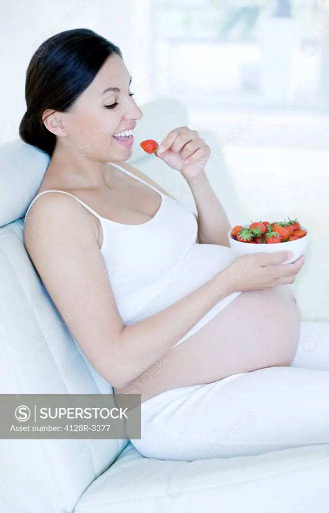 Pregnant woman eating strawberries. She is eight months pregnant.