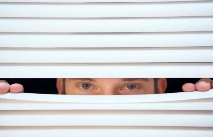 Man peeking through venetian blinds