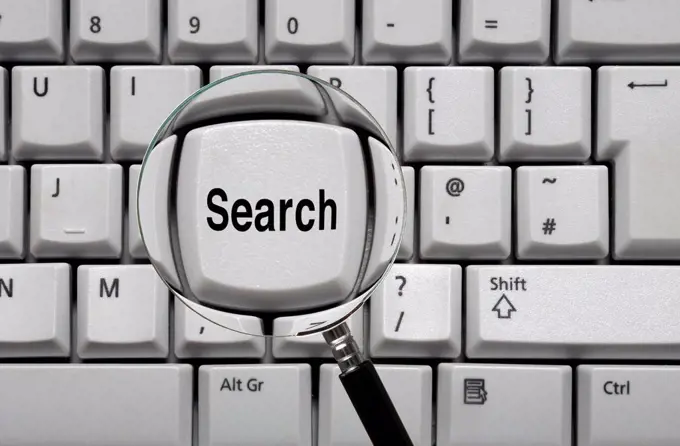 Magnifying glass over a computer key saying search.