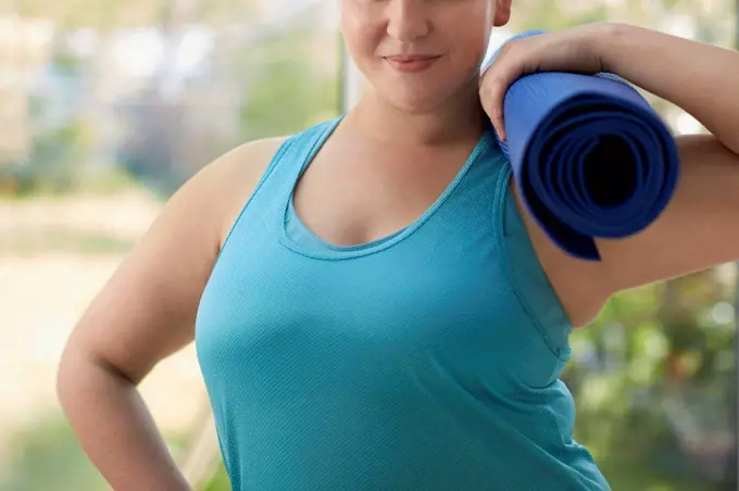 Woman holding yoga mat, cropped.