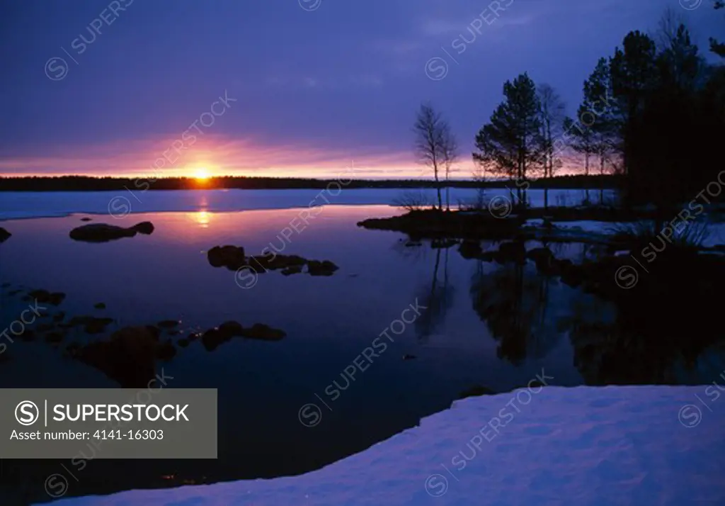 sunset over thawing lake kuusamo, finland winter